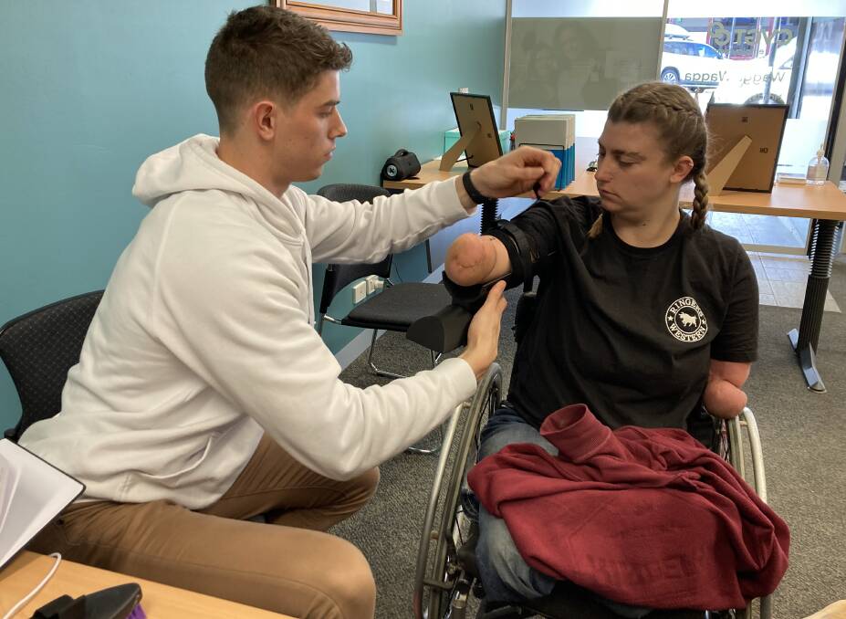 University of Wollongong student Charles Crisp fits the prosthetic device to Grace in the CVGT Employment's Disability Employment Service office in Wagga Wagga. Picture by the University of Wollongong