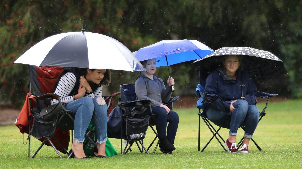 ASSISTANCE NEEDED: Saints supporters Nicole Ward, Madison White, 6, and Kirsty White take shelter from the rain under the junior softball at French Fields on Saturday.