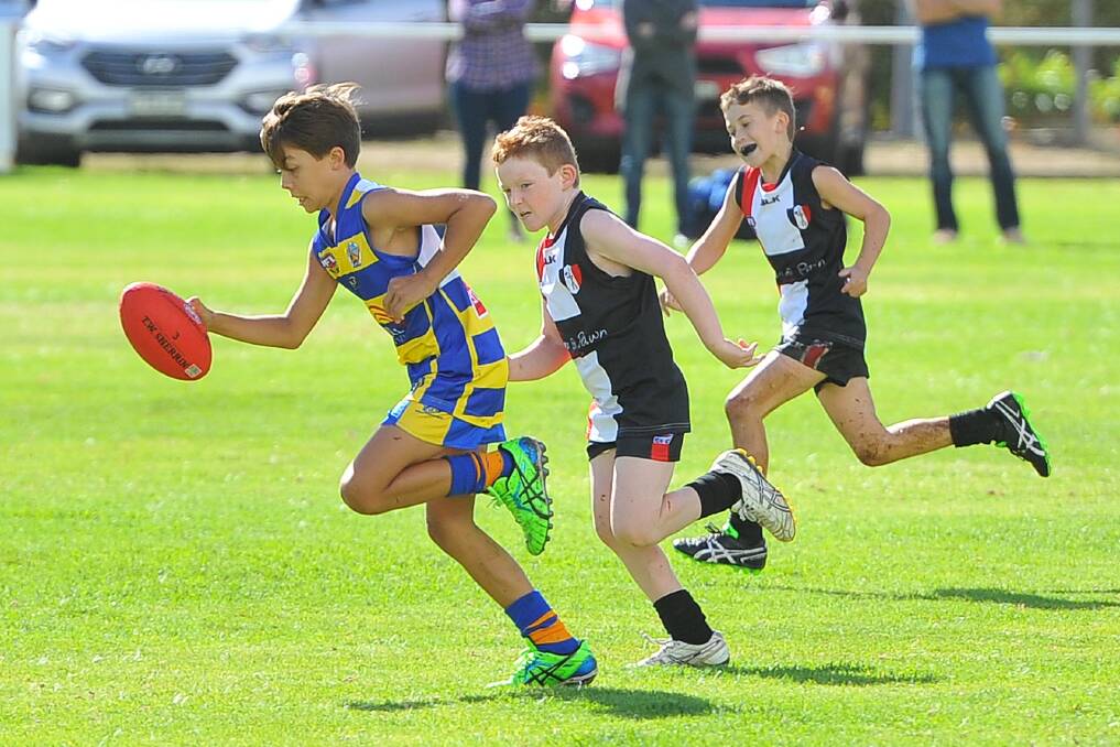 MCUE's Flynn Collins takes a bounce, leaving his North Wagga opponents behind in the under 11's junior Aussie Rules. Picture: Kieren L. Tilly