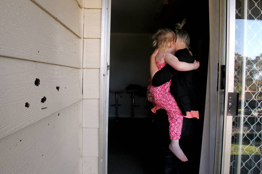 A mother and her three-year-old daughter move inside the door of a Barrack Heights home, past chipped weatherboard showing where pellets connected with the house. Picture: Sylvia Liber