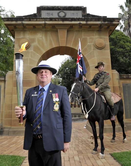 ANZAC FLAME: Brian Watts holds the RSL Anzac Flame out front of Wagga's memorial arch while in the background is Connor McComas on Jasmine. Picture: Les Smith