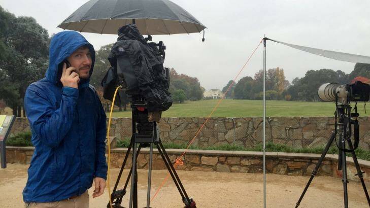 A wet and cold channel 9 cameraman wishes his mother Happy Mother's day while staking out Government House ahead of the expected arrival of Prime Minister Malcolm Turnbull. Photo: Alex Ellinghausen