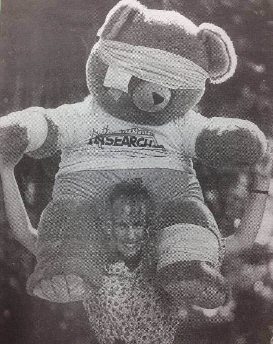 Miss Wagga entrant Belind Foulds from Youth Insearch, Wagga, gives a lift to this huge Insearch Bandage Bear at the Victory Memorial Gardens.