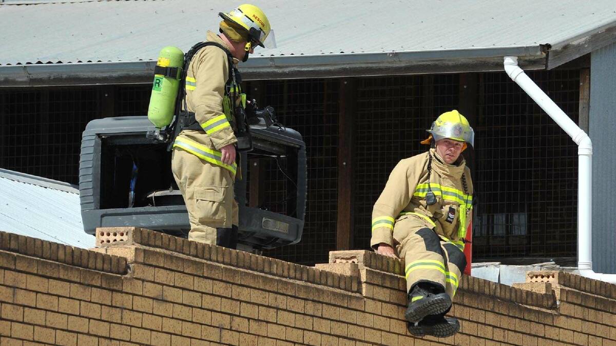 Firefighters work on the roof of the Optus shop after a fire in the airconditioner. Picture: Michael Frogley