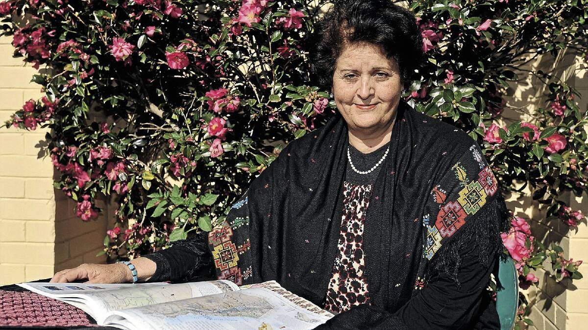 ENLIGHTENING: Dr Mona El Farra looks over the Gaza Strip in an atlas, while wrapped in embroidery made by women in Gaza refugee camps. Picture: Alastair Brook