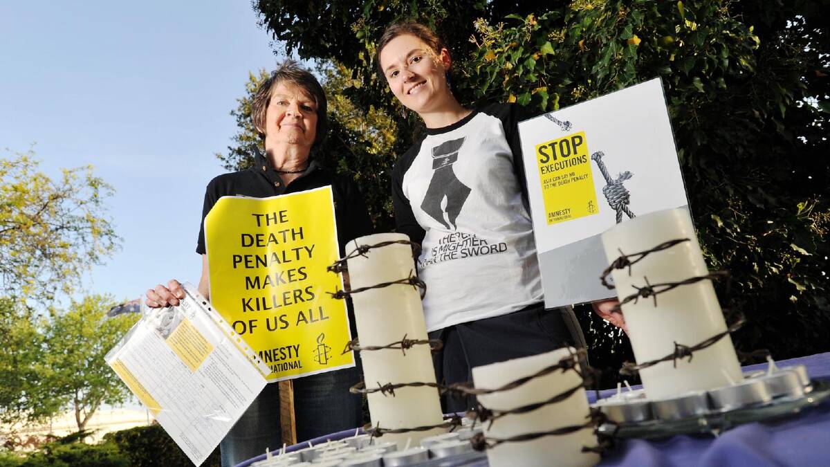 BURNING DESIRE: Convener of the Wagga branch of Amnesty International, Gabrielle Robinson (left) and event organiser Holly Wright battled the windy weather for a candlelight vigil in the Victory Memorial Gardens yesterday. Although the flames didn’t last long, the strong message saw a steady stream of people take part. 	Picture: Alastair Brook
