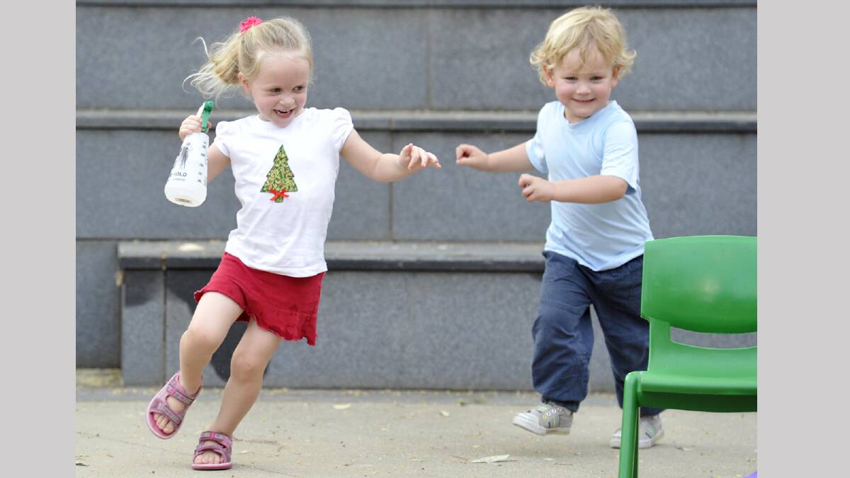 Abigail Combs and Dustyn Robbins, both 3, use a spray bottle to keep cool as they run around at Wagga's 2013 Carols in the Amphitheatre. Picture: Les Smith