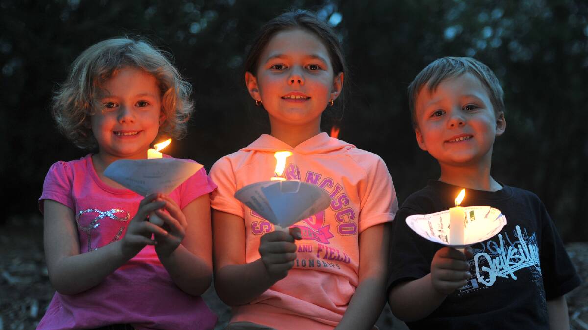 Stephanie Charlton, 5, Veronica Charlton, 9, and Kaden Lander, 5, bask in the candelight at the Christmas Spectacular at the Wagga Music Bowl. Picture: Addison Hamilton