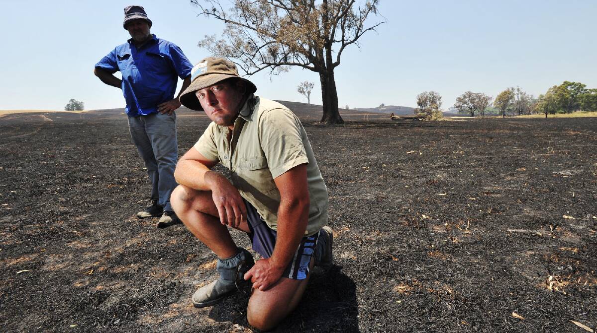 RAVAGED: James Douglas (front) and his dad, Les, stand in the burnt land of their Big Springs property. Picture: Oscar Colman