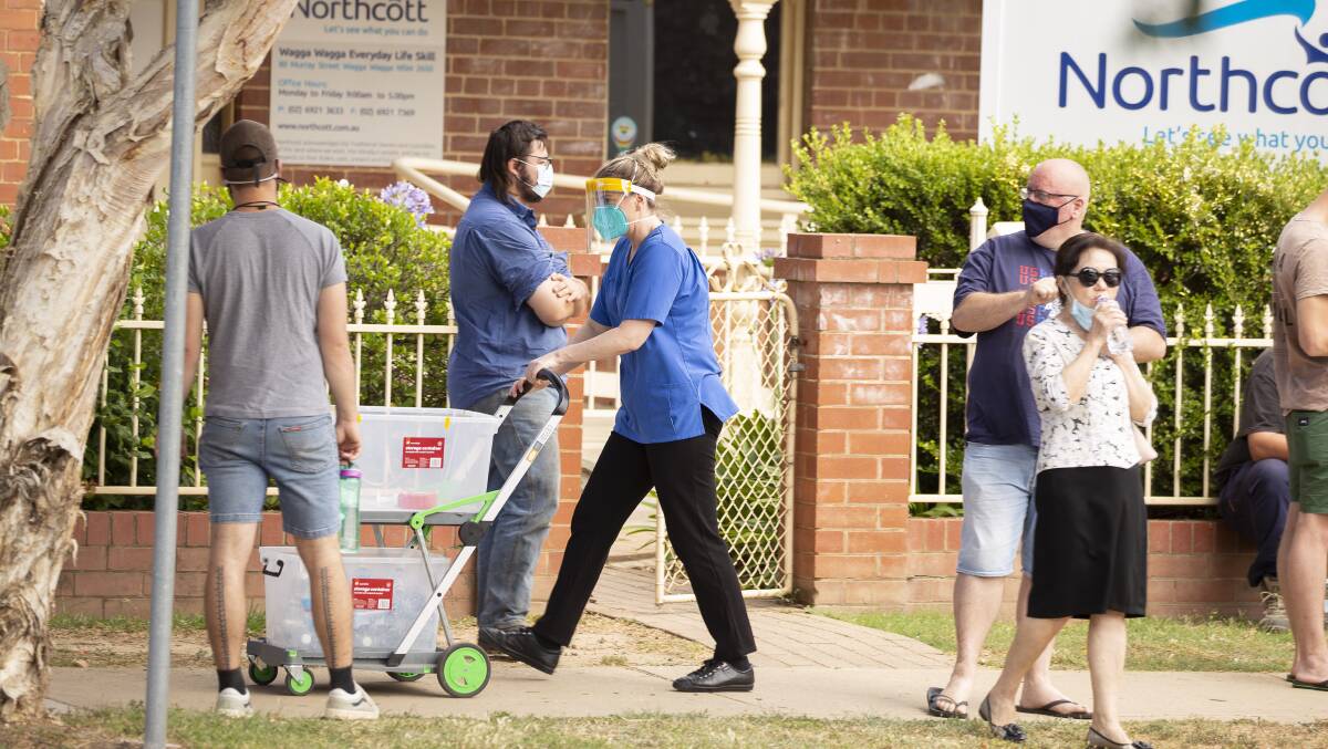 A nurse hands out water to people queuing at the Murray Street clinic. Picture: Ash Smith