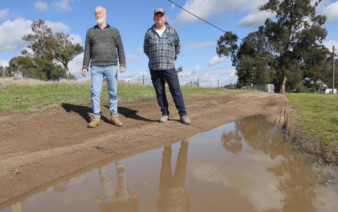 Oura residents Chris McGregor (right) and John Smart standing by one of the large potholes that make up the small village's evacuation route in early September. Picture by Les Smith 