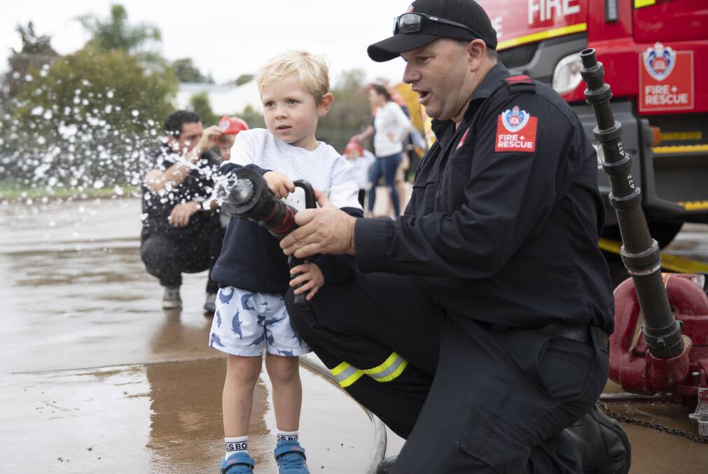 FRNSW firefighter Wayne Sanbrook helping Judd Carroll, 3, with a fire hose. Picture: Madeline Begley