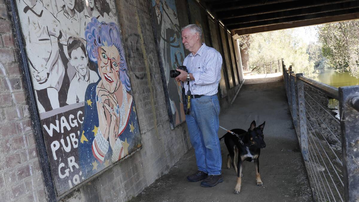 Bob Erwin and his dog Sheila pay tribute to Barry Humphries at the Dame Edna mural under Wollundry Lagoon Bridge. Picture by Les Smith 