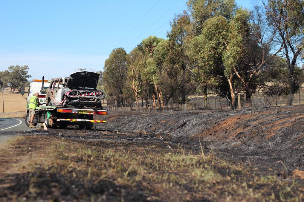 Charred remains of the Mitsubishi are removed from the burnt grasslands on the Olympic Highway near Kapooka. Picture: Emma Horn