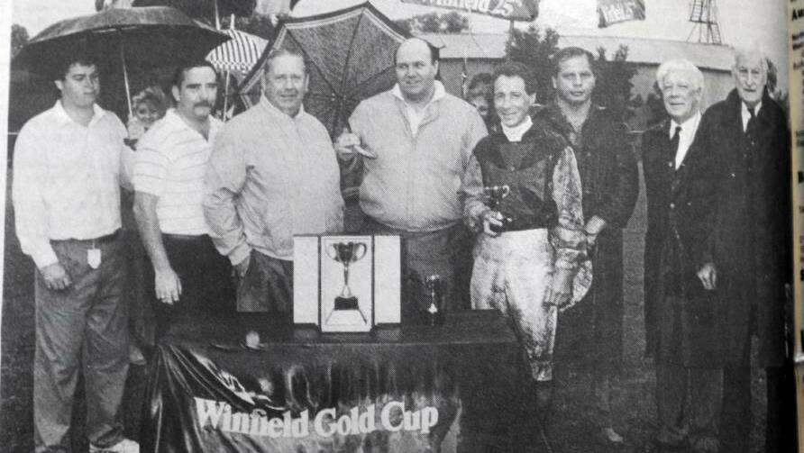 WET WINNERS: A mud splattered Denis McClune shows off his miniature trophy for winner the Wagga Gold Cup as trainer Les Edwards (third from left) and connections are presented with the $7000 trophy by NSW Minister for Sport and Recreation Bob Rowland-Smith (far right).