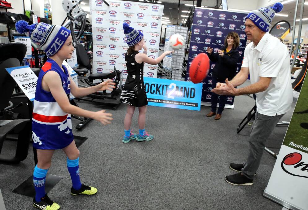 Ollie Stout, 9, and Aly Mazzocchi, 10, passing balls with Julianne Clancy and Chris Daniher wearing their Sock It To MND socks. 