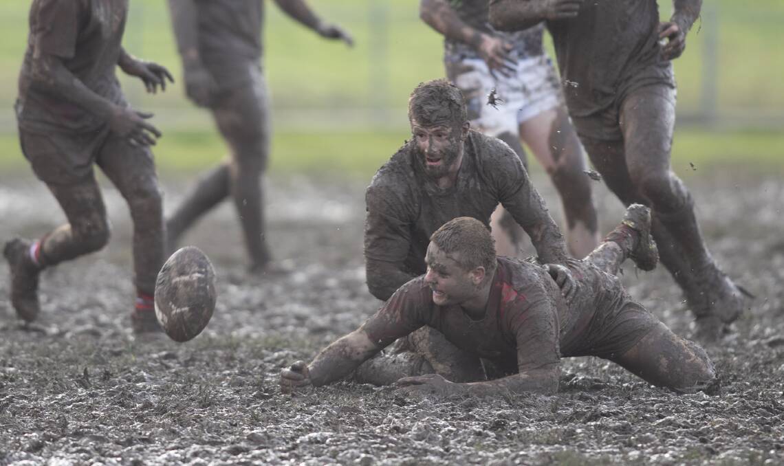 SLOGFEST: Ryan Cain tries to slip a ball backwards under pressure from Lachlan Bristow in muddy conditions at Twickenham on Sunday. Picture: Madeline Begley
