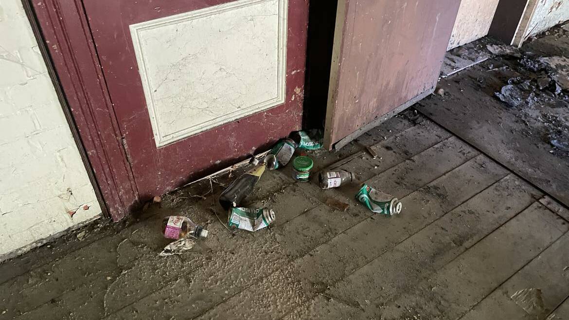 Empty alcohol bottles and cans lie around next to a boarded up doorway in the former railway barracks building. Picture supplied