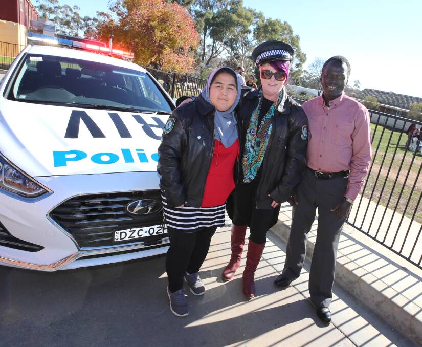 DRESS UP: Fatema Rahimi, Belinda Crain and Samson Abbas take a happy snap with police gear and car at the Refugee Week Fair. Picture: Les Smith