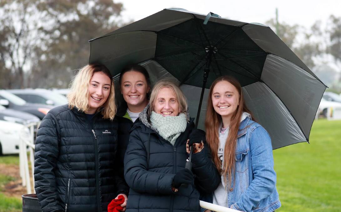 Millie Flynn with Ava, Jo and India Burkinshaw all rugged up and shielding themselves from the rain. Picture: Les