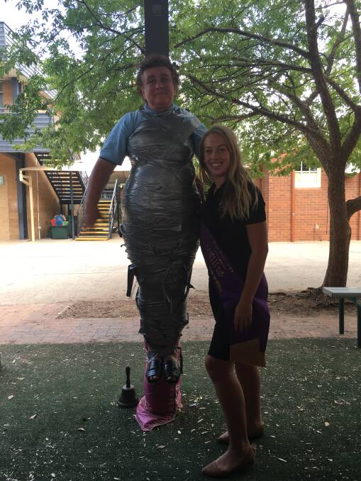 NO MOVING: St Joseph’s teacher Luisa Tavella is well and truly wrapped up as part of “tape up your teacher” in aid of Ambassador Quest entrant Madi Coelli (right). 