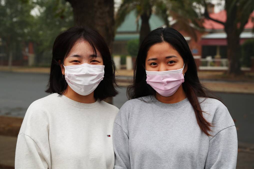 SAFETY FIRST: Korean travelers Mirim Kwon and Yurin Lee try to protect themselves from the hazardous smoke. They had been planning to spend a few months in Tumbarumba picking berries during the harvest season but instead were evacuated to Wagga. Picture: Emma Hillier