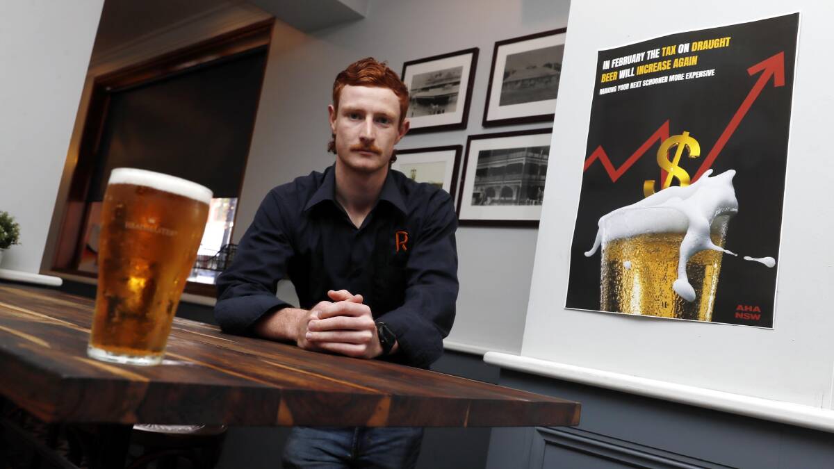Romano's Hotel bar manager Corey McConville with a poster informing pubgoers of the upcoming price hike for schooners and pints. Picture by Les Smith