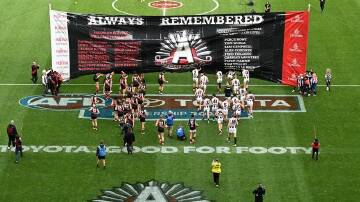 Essendon and Collingwood players run through the joint banner ahead of their Anzac Day clash. (James Ross/AAP PHOTOS)