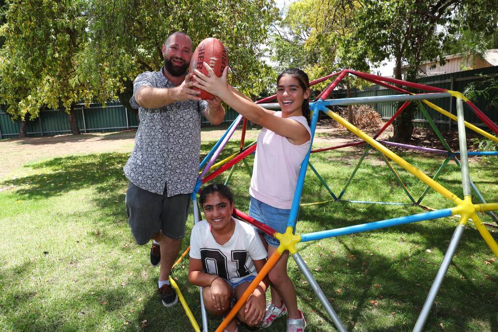 MARK: Thom Paton joins Rozaliya Hasan, 12, and Shireen Khalti, 12, to show off the skills they've learnt over the course of the AFL program. Picture: Emma Hillier