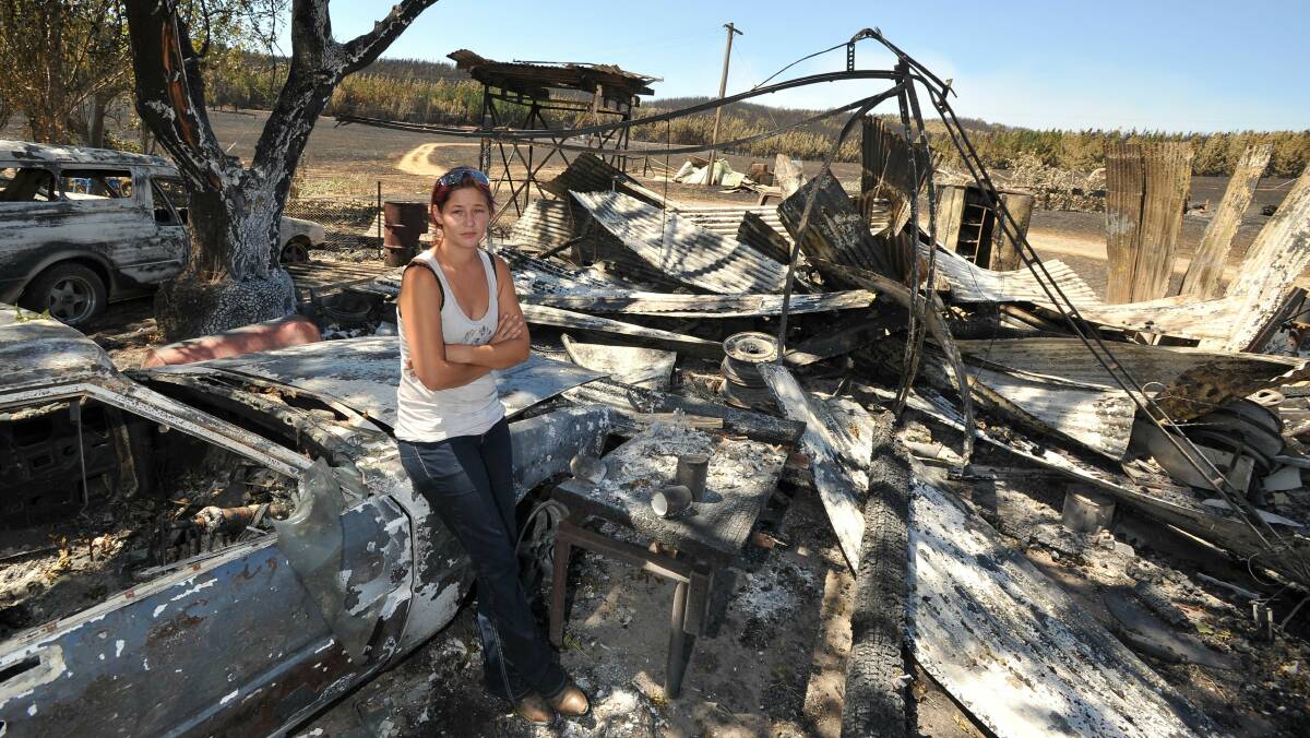 Mel Meyers sits among the remains of the family's shed and vehicles, which were destroyed by the Minnimbah fire on Saturday. Picture: Michael Frogley
