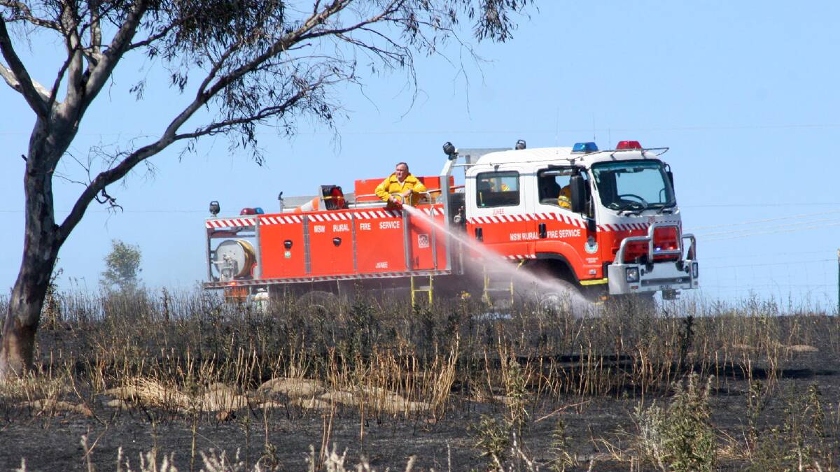 Firefighter mop up a blaze in a Junee paddock caused by a tractor slashing grass. Picture: Declan Rurenga