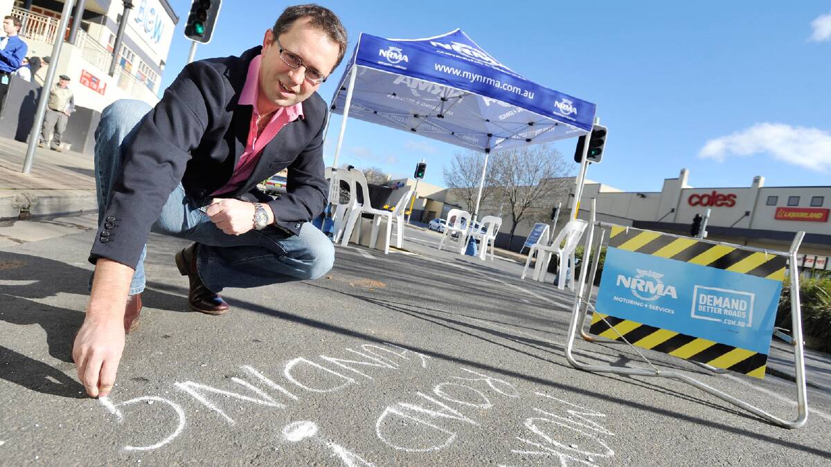 Councillor Julian McLaren adds his message to the NRMA chalk petition on Forsyth Street. Picture: Alastair Brook